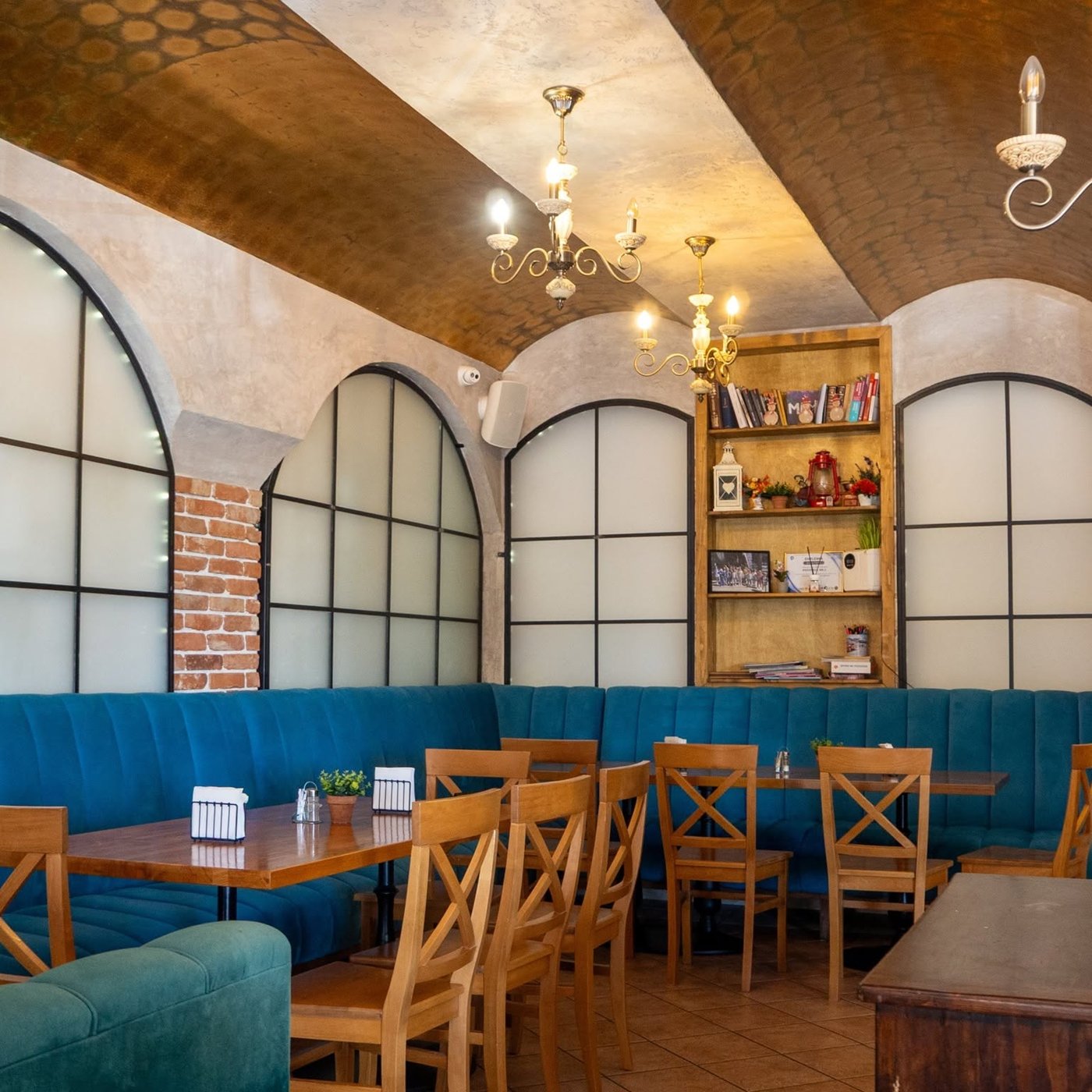 Salonul pizzeriei, cu bolți, candelabre, bibliotecă și canapele albastre